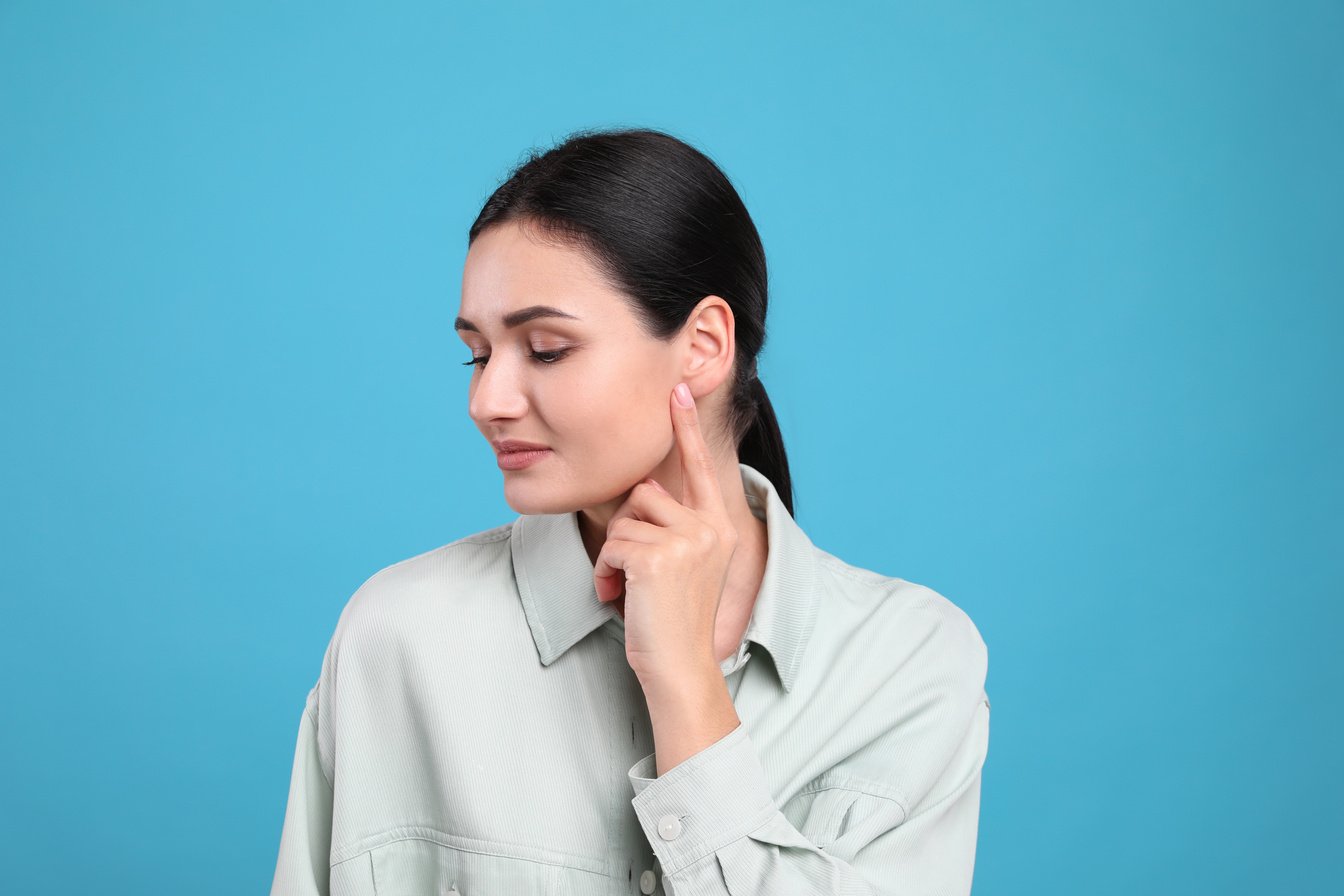 Young woman pointing at her ear on light blue background